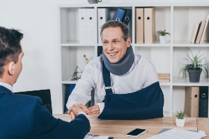 worker in neck brace with broken arm and businessman in blue jacket shaking a lawyers hands